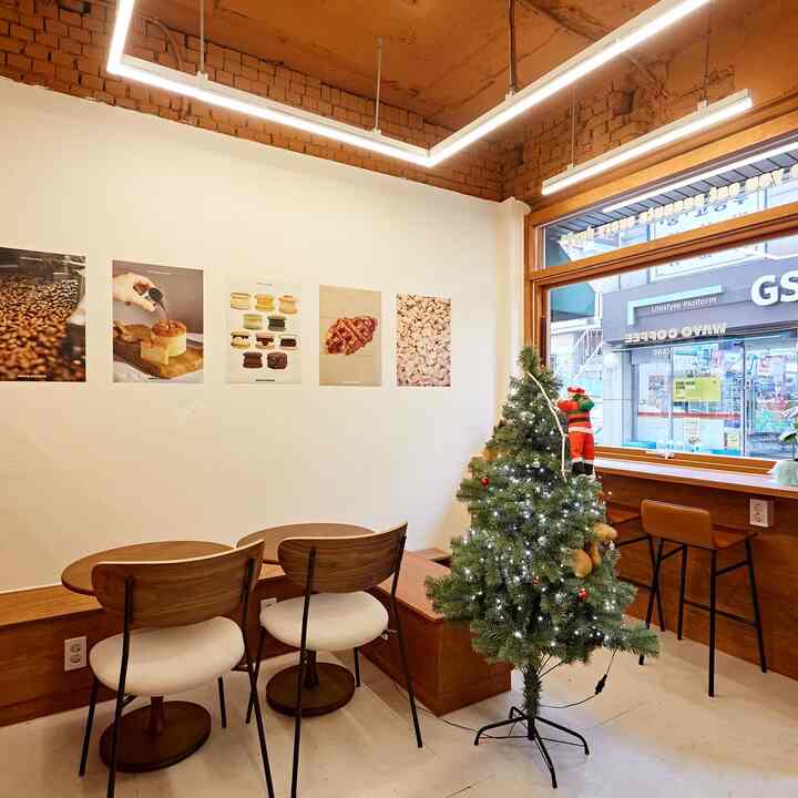 白い壁と茶色の木製家具が調和したカフェ風の空間、窓際のバースツールとクリスマスツリーが配置された温かみのあるインテリア