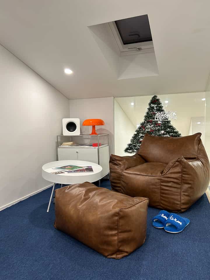 ブラウンのレザーのビーズクッションとオレンジ色の照明が配置されたロフト、ブルーカーペットで暖かみのある雰囲気のインテリア