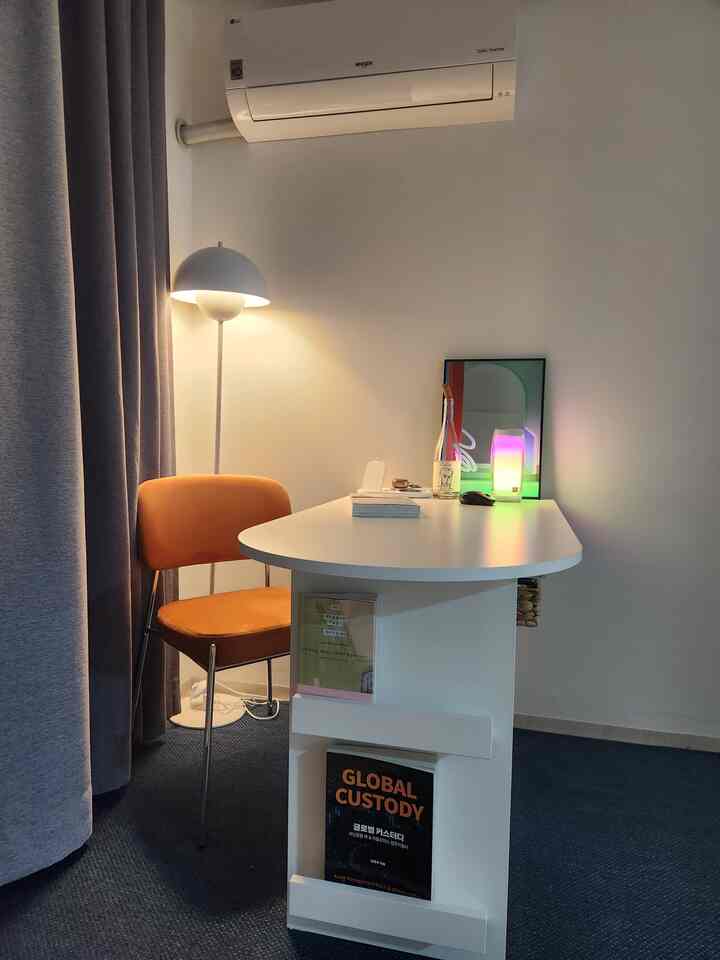 White and gray toned small home office space featuring orange chair and white desk with modern, minimal style
