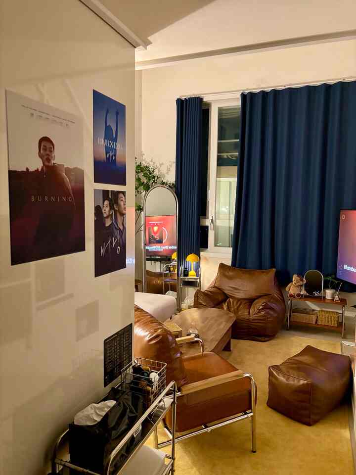 ブラウンのレザーのビーズクッションと椅子、ネイビーのカーテンが調和したワンルームのリビング