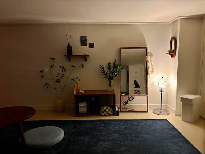 ナチュラルな色調の寝室、木製の棚とフロアランプが配置された落ち着いた印象のインテリア