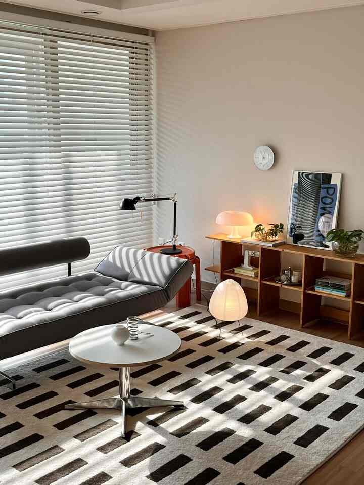 白とグレーの色調のリビング、円形テーブルとソファベッド、木製の棚と照明が配置された落ち着いた空間