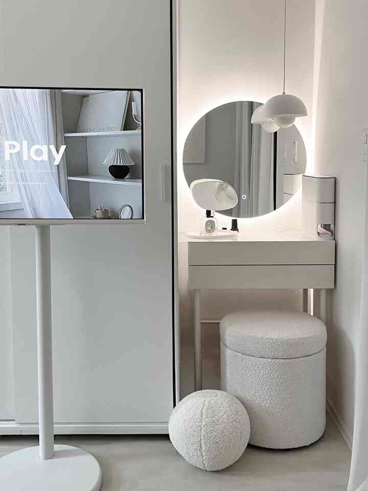 White-toned living space featuring a vanity with LED backlit round mirror and a soft-textured vanity stool, presenting a modern ambiance