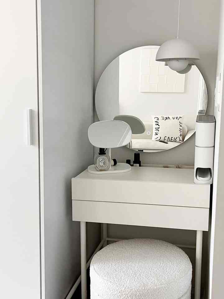 A compact, white-tone powder room featuring a large round mirror and a neat vanity in a simple and modern style