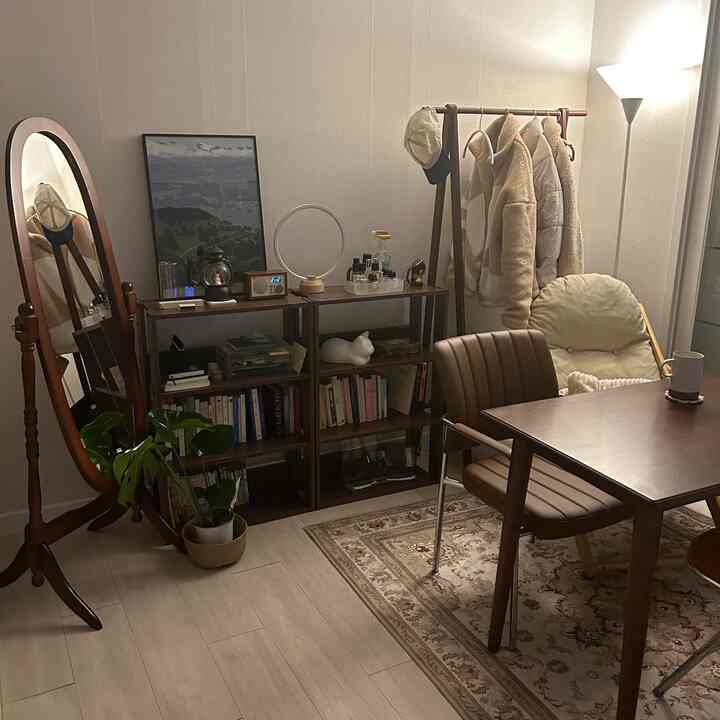 温かみのある木目調のリビング、ダイニングテーブルと椅子、全身鏡、棚、ハンガーラックが配置された雰囲気のあるインテリア