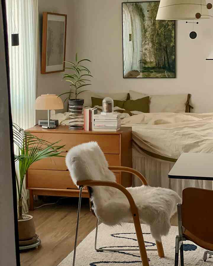 A beige and natural wood tone bedroom featuring a wooden dresser and a white fur-covered chair creating a cozy atmosphere.