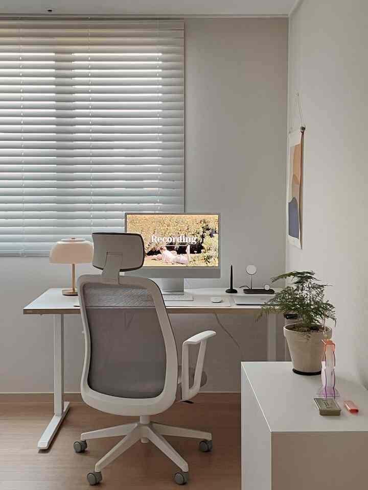 Bright white and beige toned home office featuring a central monitor and ergonomic office chair in a clean work setup