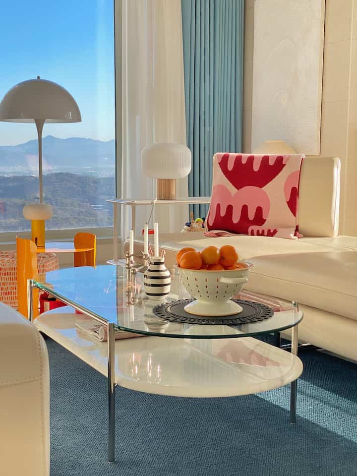 Bright white and blue toned living room featuring large window, mid-century modern sofa, and glass coffee table creating a cozy atmosphere