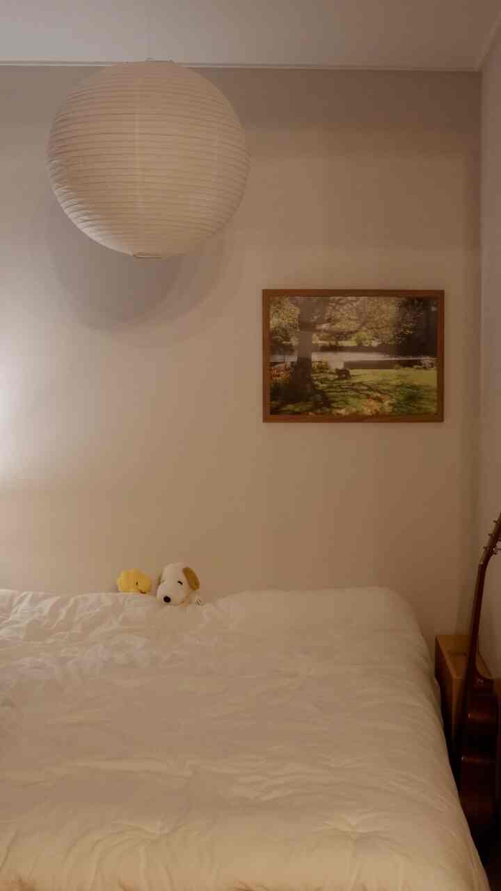 ナチュラルな色調の寝室、白い寝具と木製のナイトテーブル、壁に掛けられた絵が温かみのある雰囲気を演出するインテリア