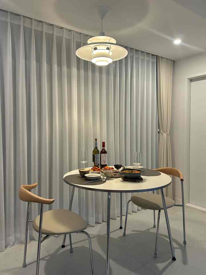 白とベージュの色調のリビング、円形のダイニングテーブルとアームチェア、ペンダントライトが配置されたシンプルでモダンな雰囲気のインテリア