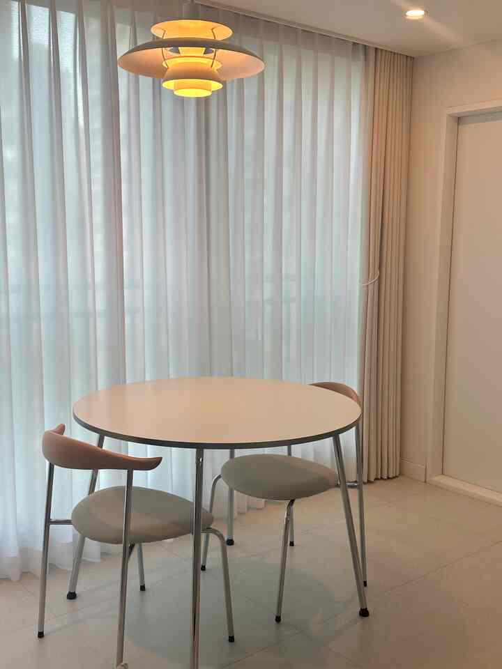 ホワイトとベージュのトーンが使われたリビングルーム、クロム脚の円形テーブルとミッドセンチュリーモダンの椅子が配置されたシンプルな空間