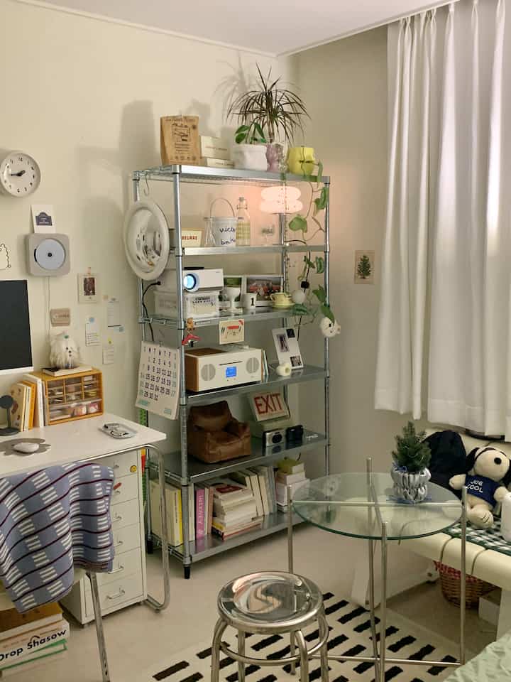 White-toned small bedroom featuring metal shelving and plants with a modern and organized atmosphere