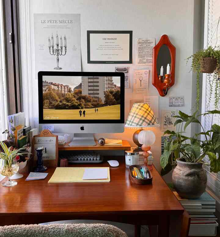 温かみのある木目調のホームオフィス、デスク中央にモニターとヴィンテージのテーブルランプ、緑豊かな植物が配置された雰囲気のあるインテリア