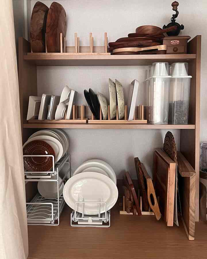 ナチュラルな色調のキッチンの棚、皿や木製まな板、透明な収納容器が整頓された清潔な収納スペース