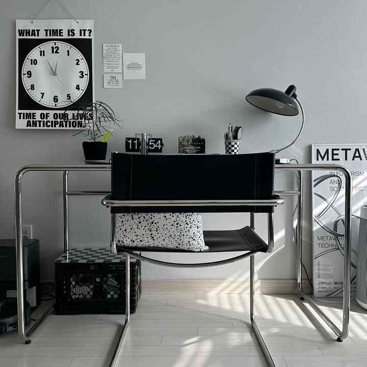 Mid-century modern home office with gray walls and light wood flooring, featuring black pipe-frame desk, leather chair, and task lamp in a neat workspace