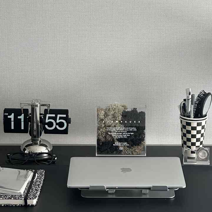 Black and silver toned home office desk featuring a retro flip clock, MacBook Pro laptop, and checkerboard pen holder in a tidy modern workspace
