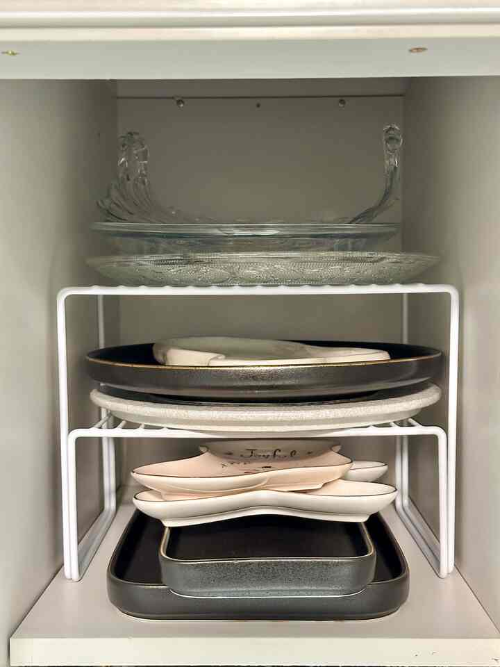 White wall cabinet interior featuring neatly organized black, white, and transparent plates on a plate rack