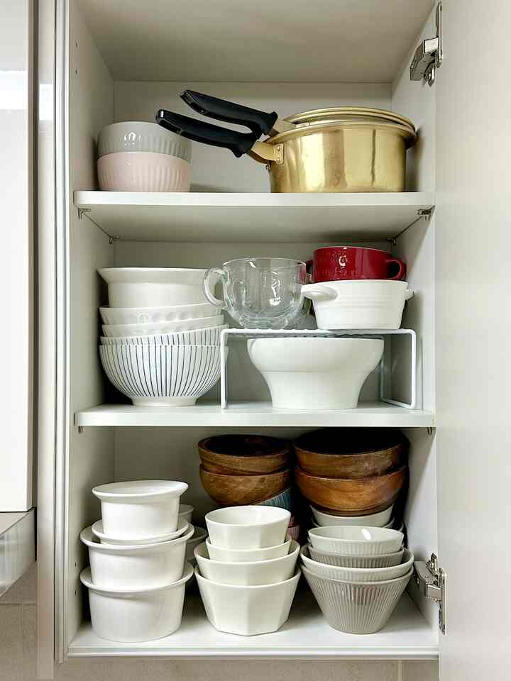 白と木目調の器がきちんと収納されたキッチンキャビネット内の整然とした収納空間