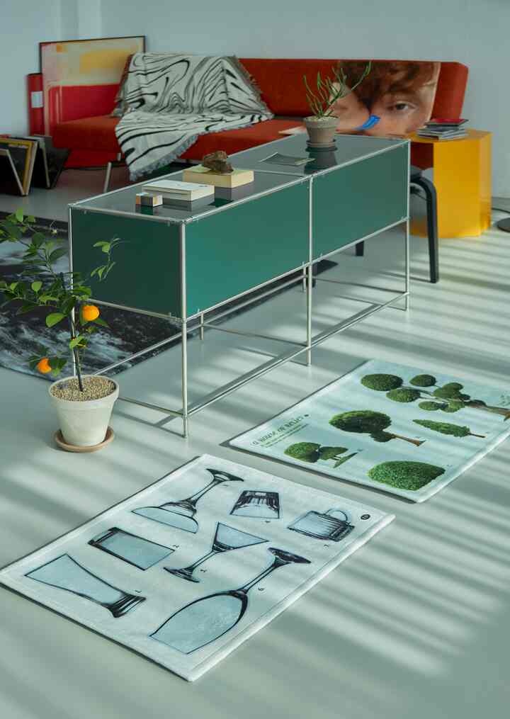 黄色とオレンジのトーンのワンルームリビング、オレンジ色のソファと黄色のサイドテーブル、植物とパターンラグが配置された明るく自然な空間