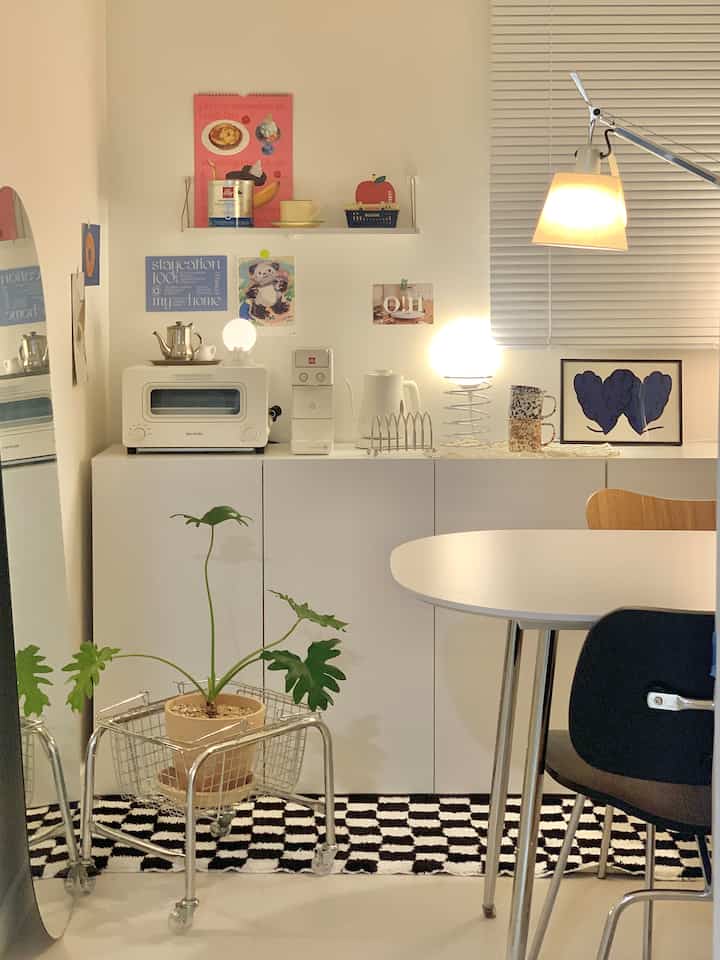 白とモダンな雰囲気のホームカフェゾーン、キャビネットとダイニングテーブル、照明、植物が配置された印象的な空間