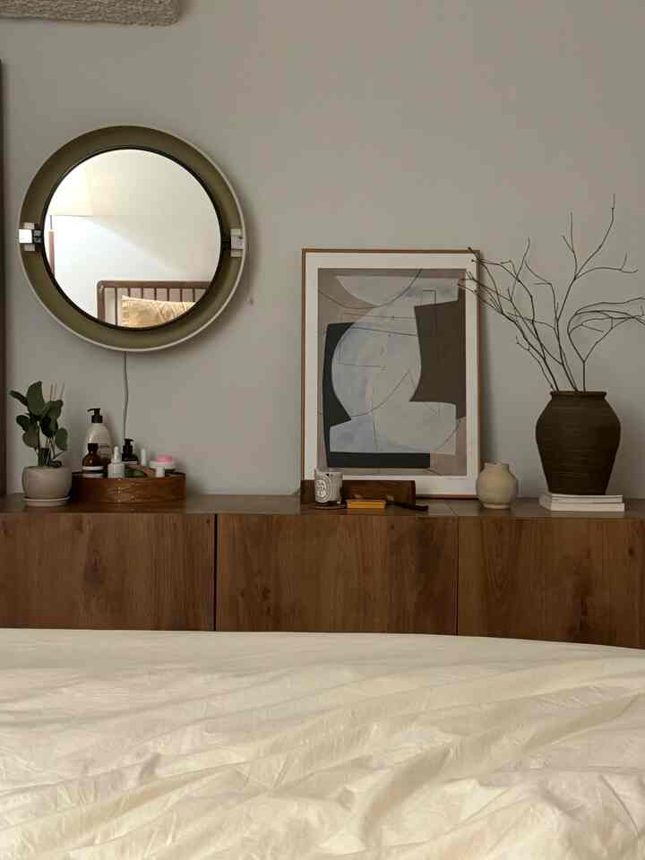 ウッドトーンとホワイトが調和する寝室、丸い鏡と抽象画の額縁が配された落ち着いた自然な雰囲気のインテリア