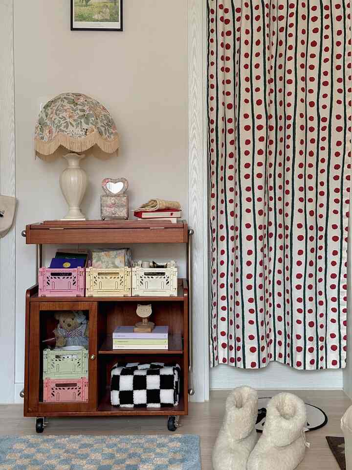 Beige-toned wall and wooden dresser form a cozy cafe style corner, complemented by red polka dot curtains and blue checkered rug