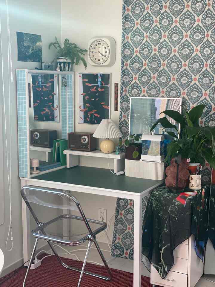 Minimal home office space featuring blue-green patterned wallpaper, white desk, vintage radio, and cream table lamp