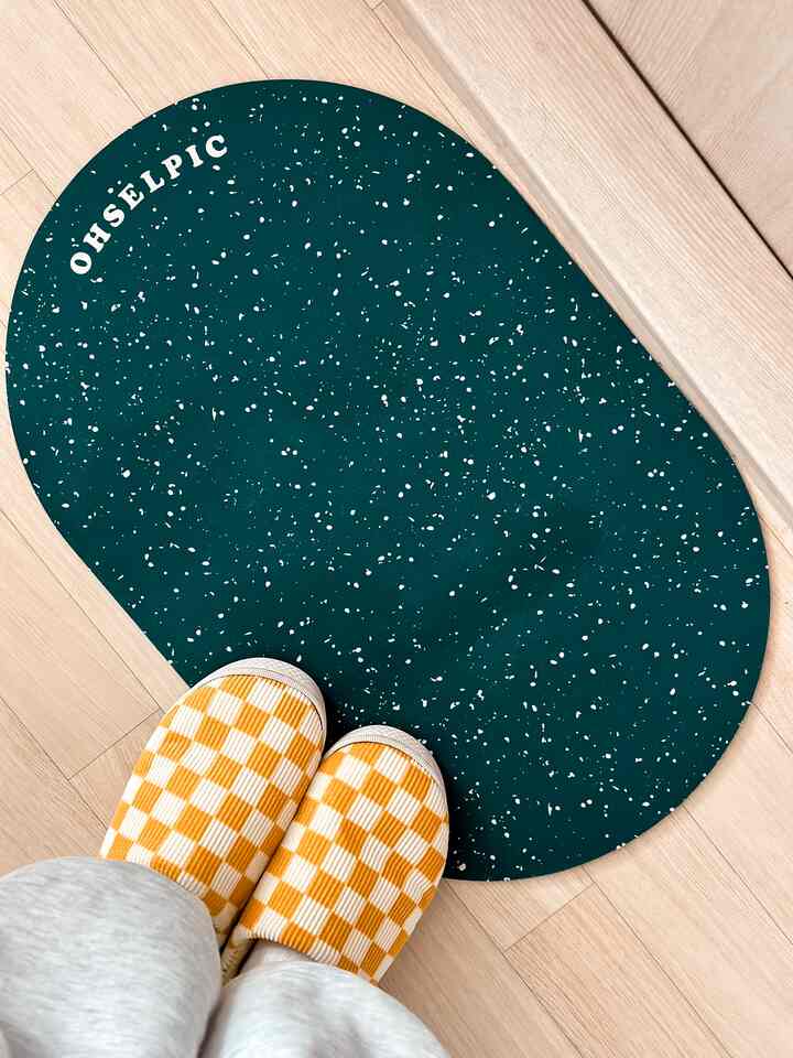 ビビッドなダークグリーン色の珪藻土バスマットと黄色のチェック柄スリッパが置かれた木目調の床の空間