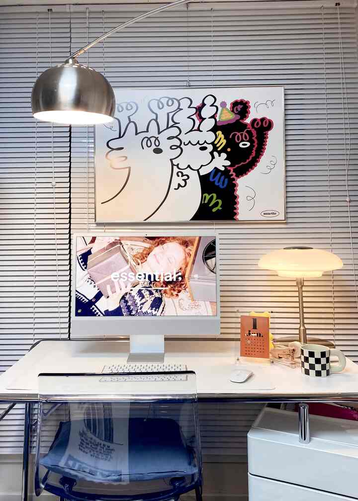 White-toned home office space featuring an iMac, clean desk, and cute illustrated picture frame in a simple modern desk interior