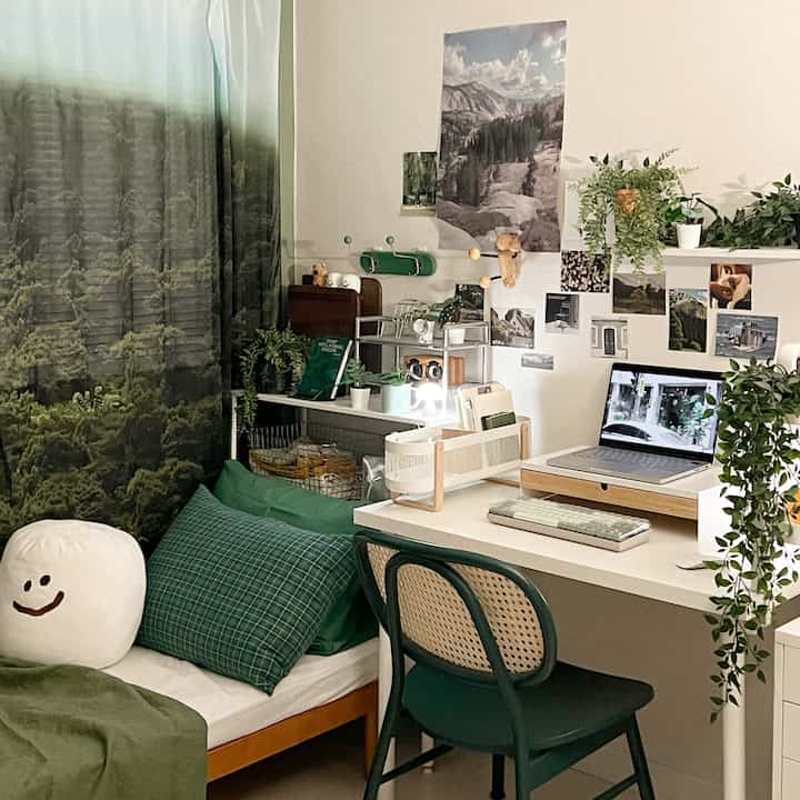 緑色のトーンが特徴の一人用ホームオフィス、植物とファブリックポスターが調和した印象的なデスクとベッドの配置