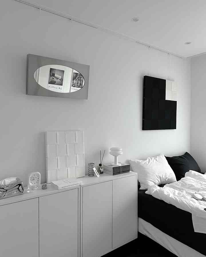 Simple modern bedroom in white and black tones featuring decorative art and mirror on the wall, with a clean and minimal atmosphere