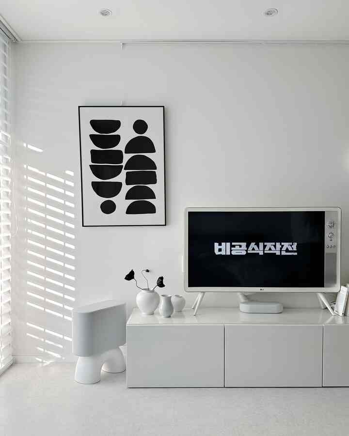 White-toned living room featuring a simple TV stand, picture frame, and accessories in a clean interior space