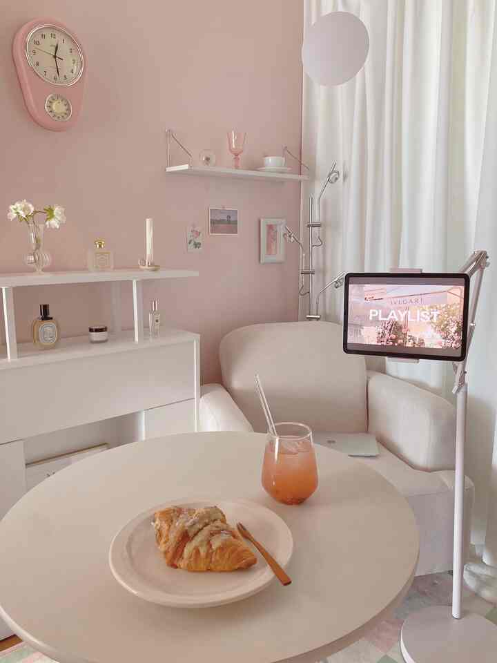 ピンク色の壁と白い家具が調和した小さなホームカフェ空間、円形テーブルにデザートと飲み物が置かれた雰囲気のあるインテリア
