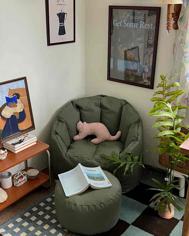 Natural toned small living room corner featuring dark green bean bag and stool with cozy wall art and plants