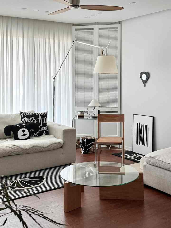 Simple modern living room with white and wood tones, featuring a beige sofa and glass coffee table in a cozy atmosphere