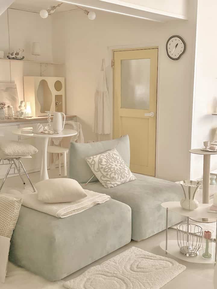 White and natural-toned living room featuring a light green sofa and unique wall clock creating a calm interior ambiance