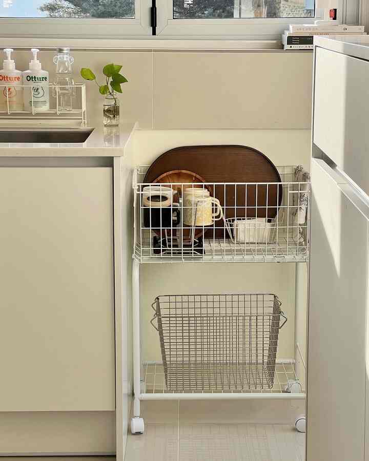 ホワイトと木目調の色合いが特徴の狭いキッチン、棚にカップとトレイが整然と配置された雰囲気のあるインテリア