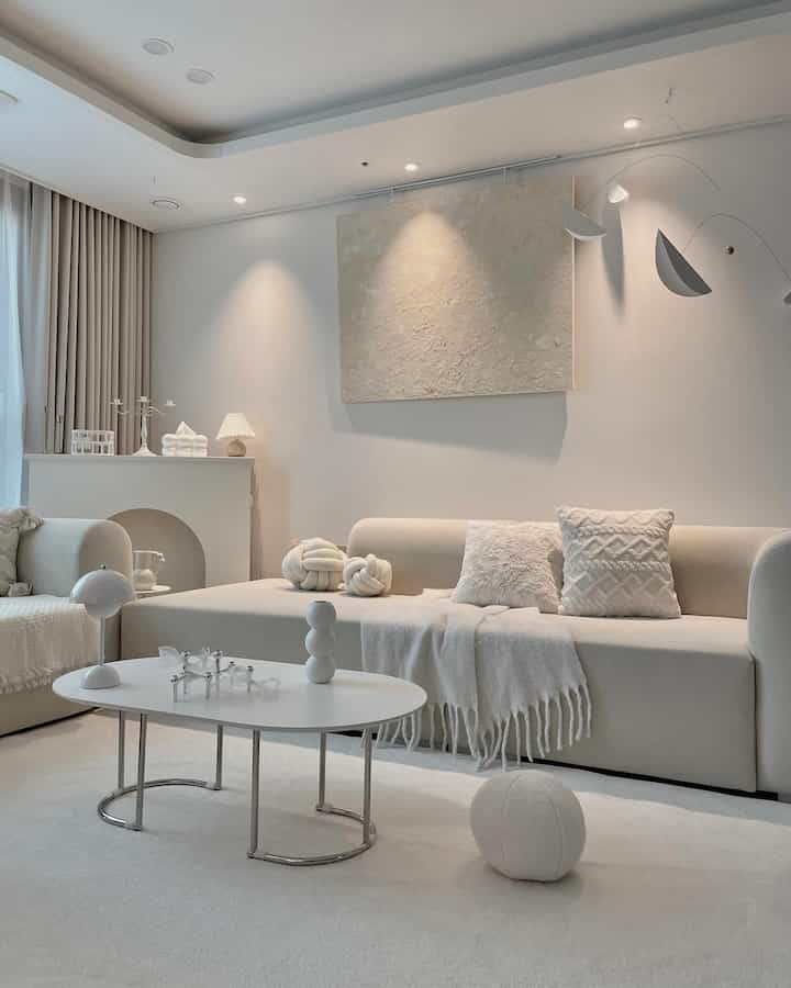 A white and beige toned living room featuring a modern sofa and coffee table with a simple and cozy ambiance