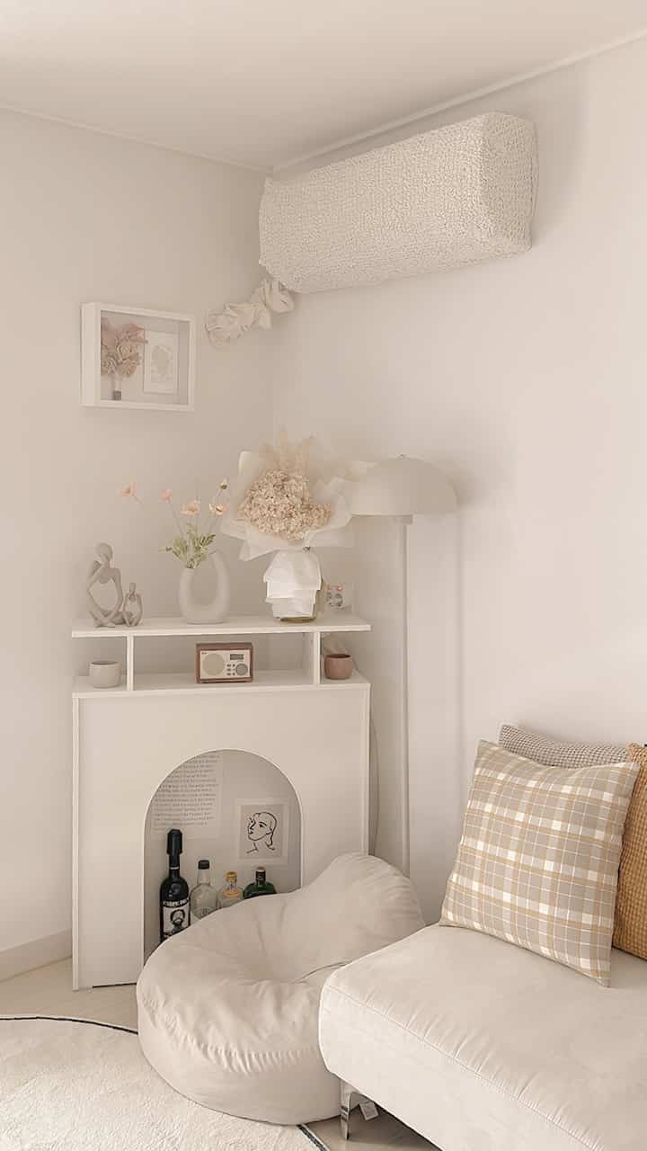 暖かいベージュとホワイトの色調のリビング、ベージュのビーンバッグとソファ、暖炉の棚とコンソールが配置されたシンプルで自然なインテリア