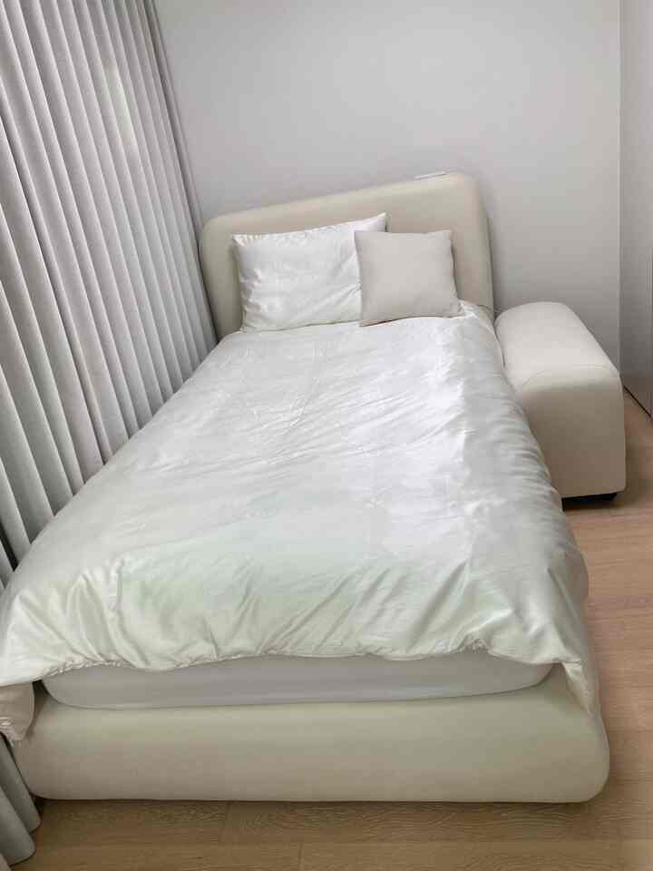 ホワイトと木目調が調和したコンパクトな寝室、柔らかな曲線のベッドフレームと遮光カーテンが配置された清潔感のあるインテリア