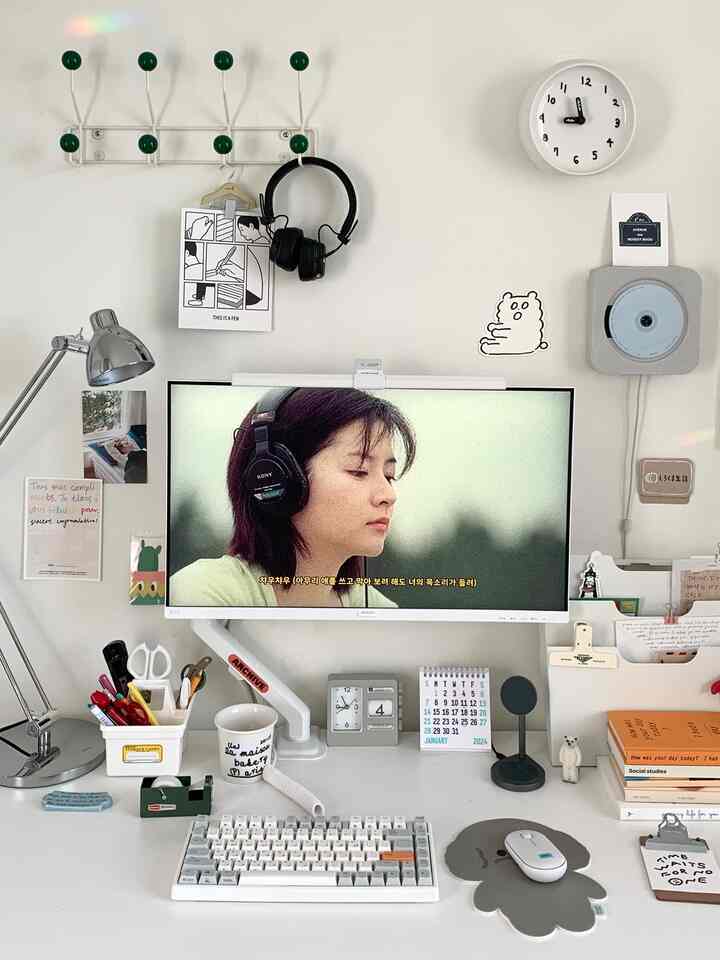 White-toned home office featuring a clean desk with monitor, white keyboard, desk lamp, and black headphones creating a calm atmosphere