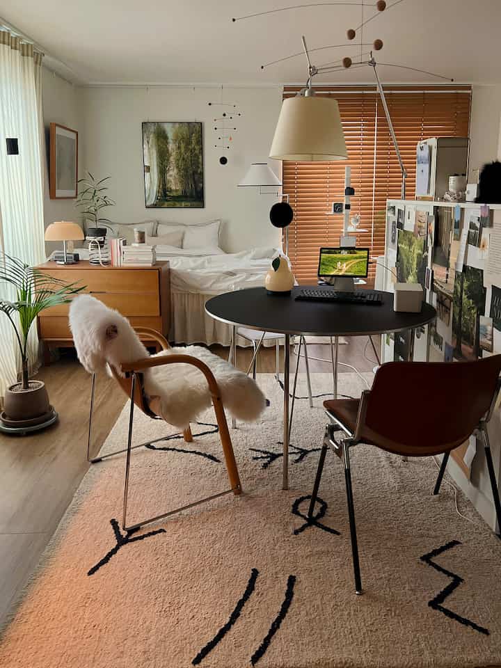 Light brown wood tone studio apartment bedroom featuring table lamps and plants, with a cozy and warm atmosphere