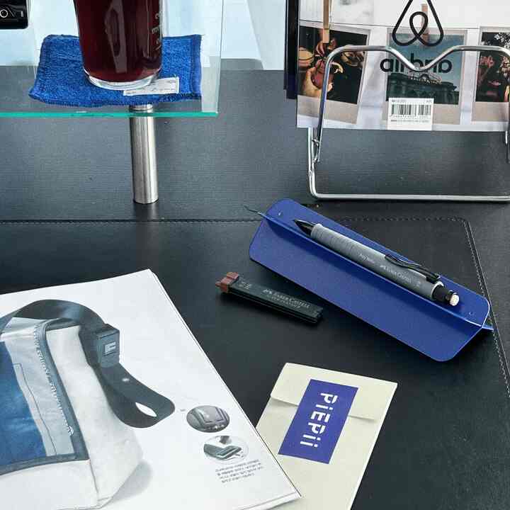 Black and blue toned desk space featuring desk mat, monitor stand, and writing tools in a tidy study setup