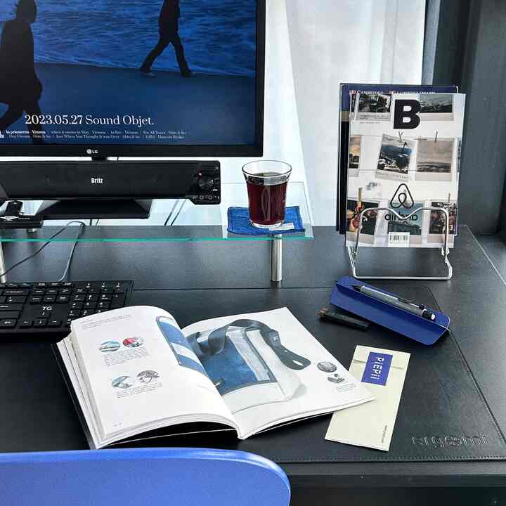 黒を基調としたホームオフィス、机の上にはモニタースタンドや雑誌、整頓されたデスクセットアップが配置された雰囲気のあるインテリア