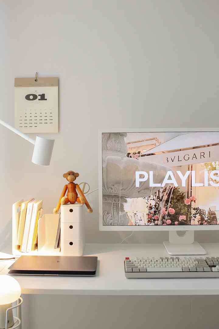 White-toned home office space featuring a monitor, desk, and wooden monkey objet, with a simple and clean atmosphere