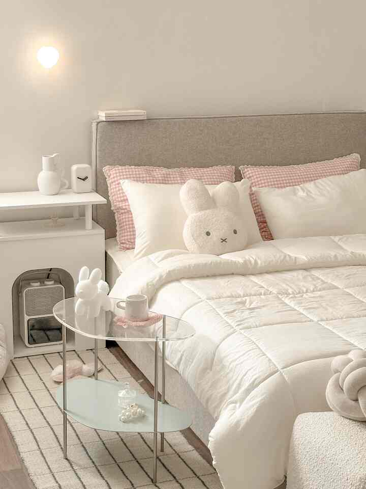 Soft white and gray toned bedroom featuring a neat bed, rug, and cute plush toys creating cozy, natural atmosphere
