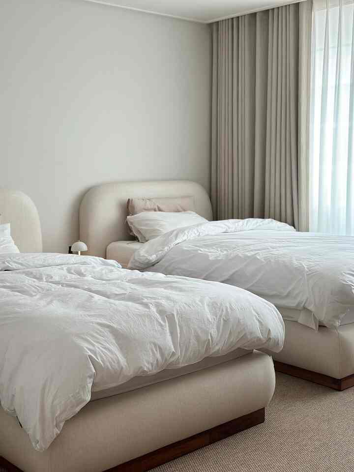 A simple and bright bedroom featuring beige and white twin beds with matching curtains