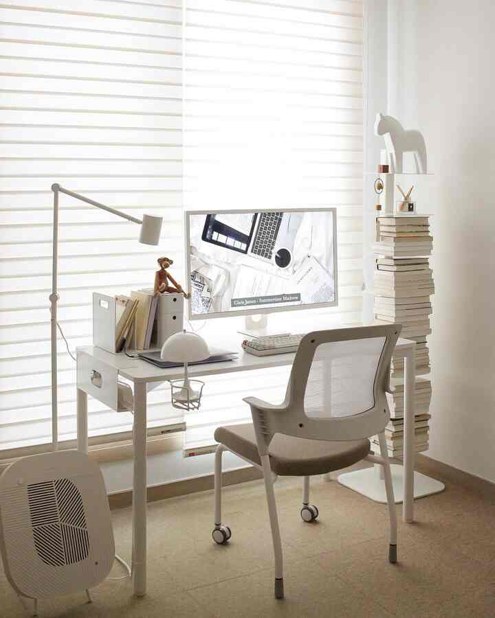 Bright white and beige toned study featuring a desk with monitor and stacked books, creating a clean work atmosphere
