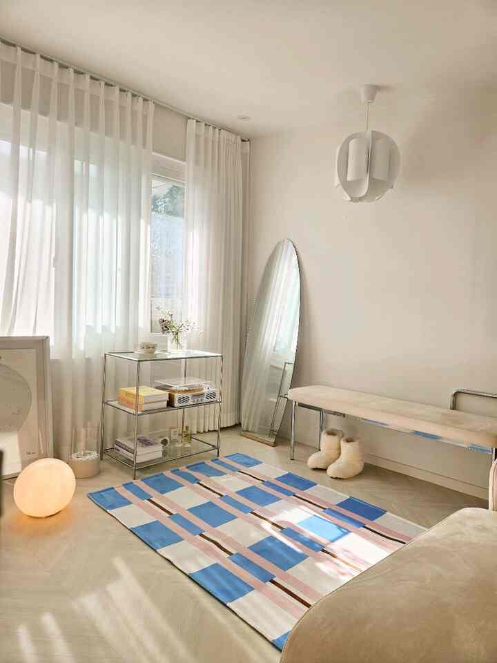 White and natural wood-tone balcony space featuring bench, full-length mirror, and colorful rug with a modern, airy atmosphere