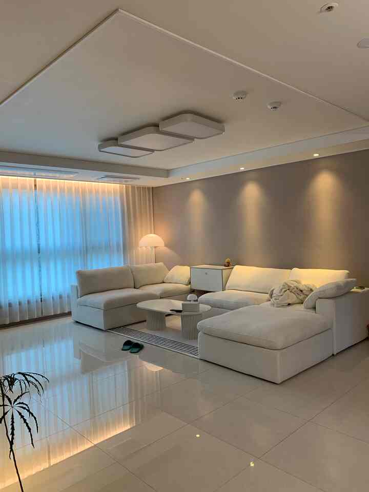 ホワイトとベージュトーンのモダンなリビング、白い大型コーナーソファと大理石タイルの床が配置された落ち着いた空間